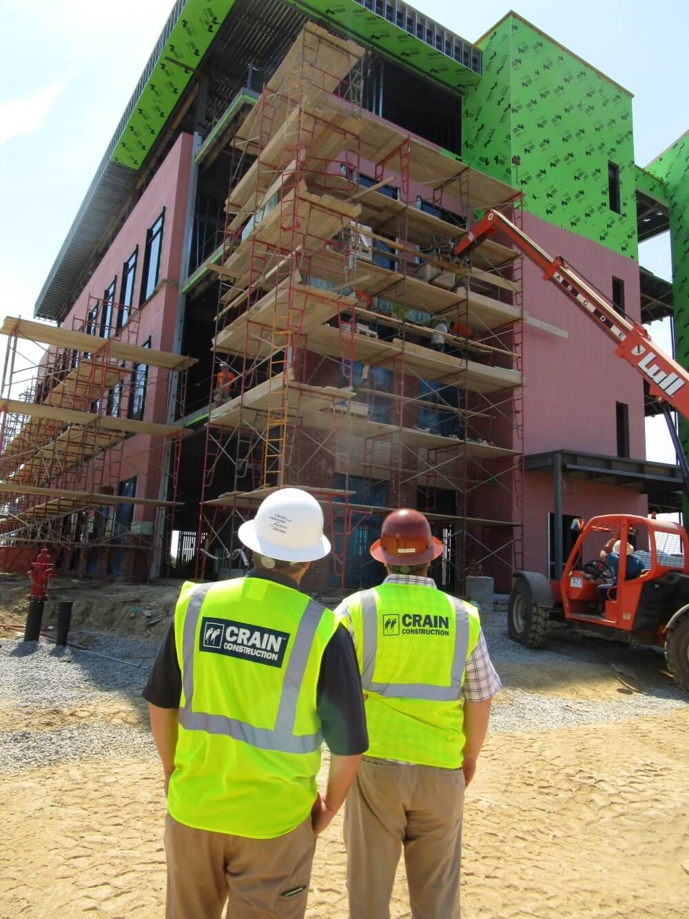 Two construction workers looking at a building that has been wrapped in weather-protecting materials