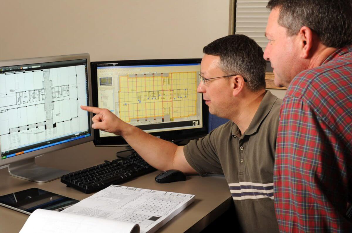 A contractor and an architect discussing a project while pointing at a computer.