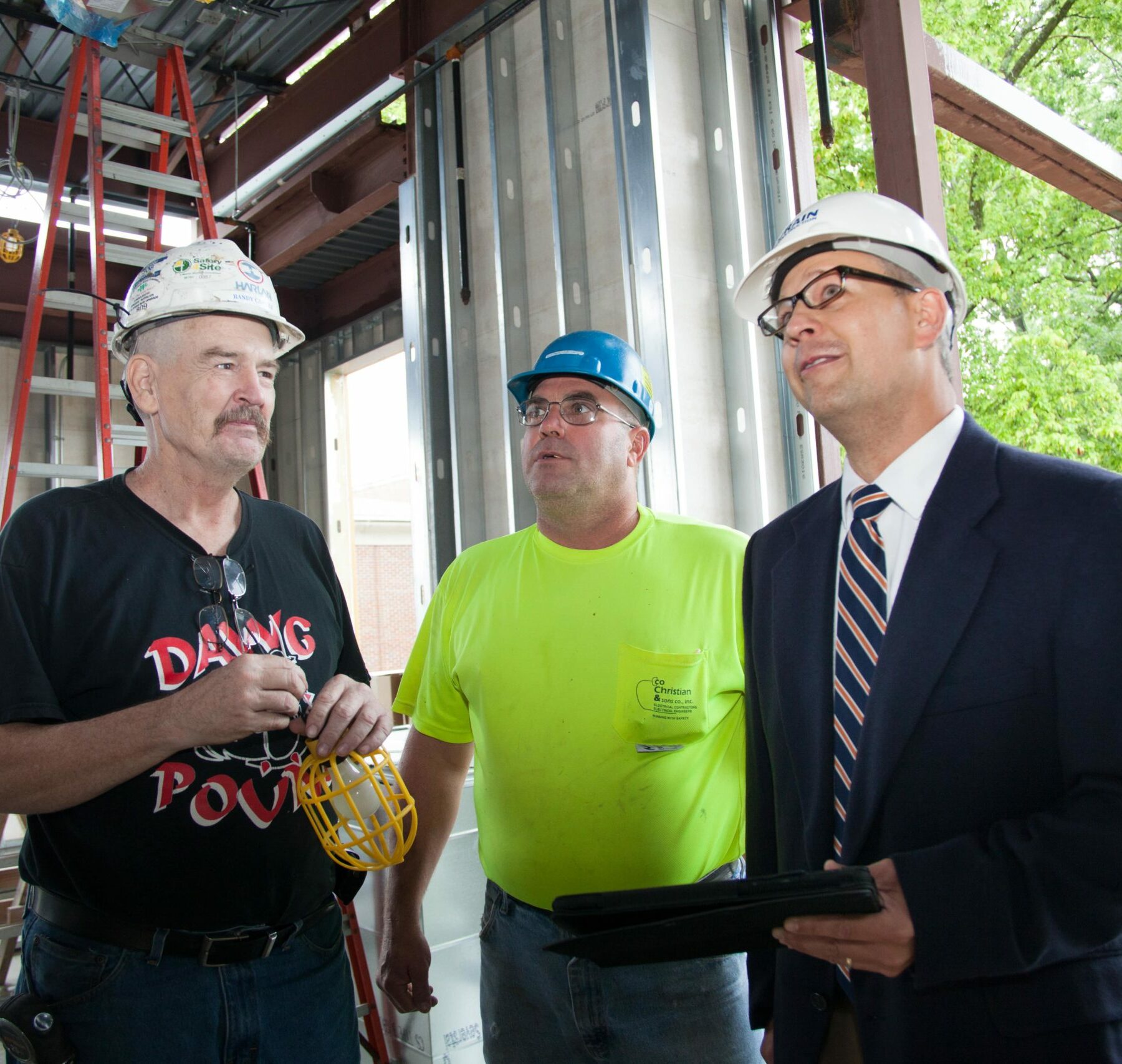 1 project manager with an iPad and 2 construction employees stand together in a construction site