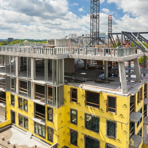 Commercial building under construction with house wrap and metal framing partially complete.