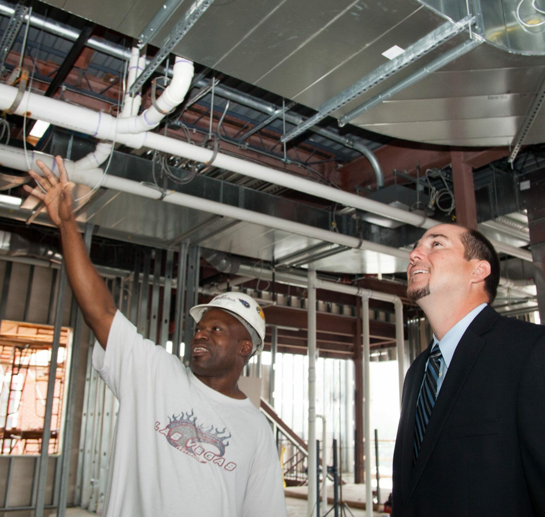 construction worker with hardhat showing project under construction to man in suit