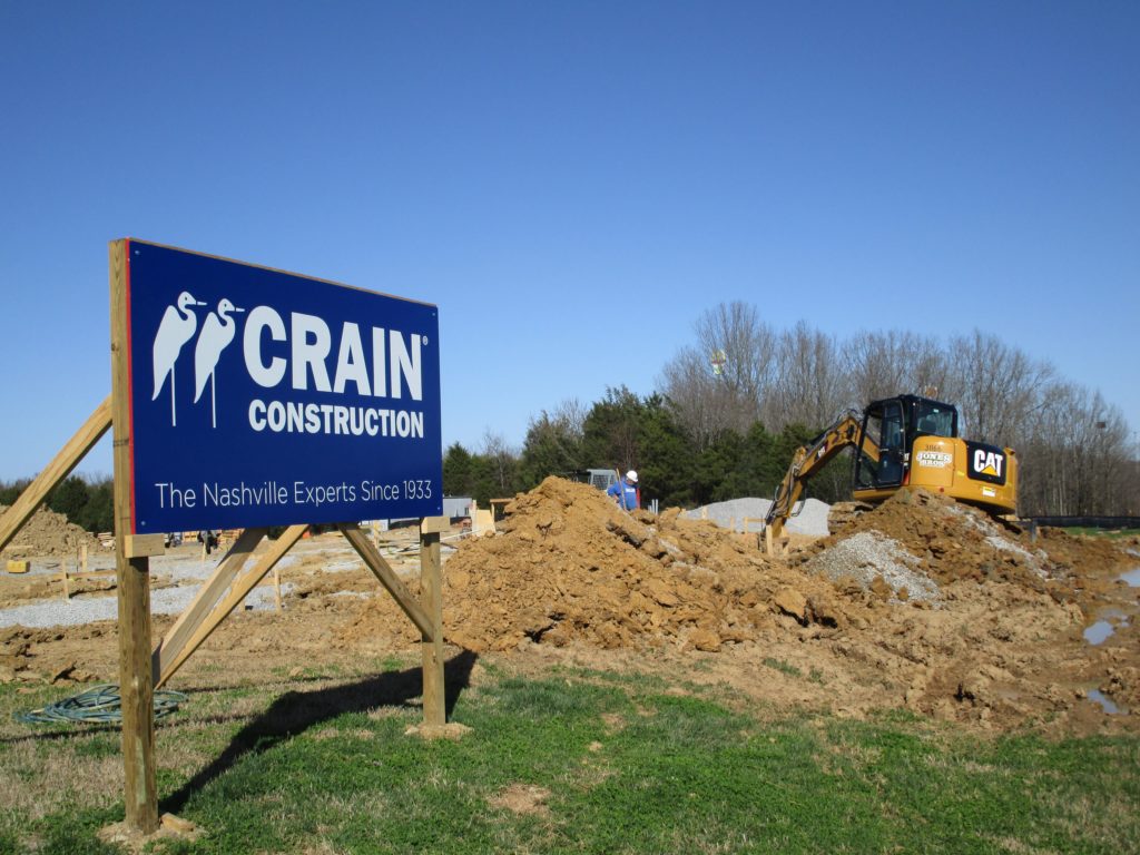 A Crain Construction sign on an active jobsite with dirt work going on behind it.
